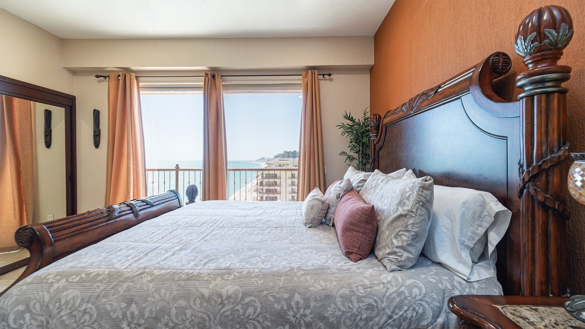 Ein Hotelzimmer mit einem großen Bett, einem hölzernen Kopfteil, einer Topfpflanze und Blick aufs Meer.