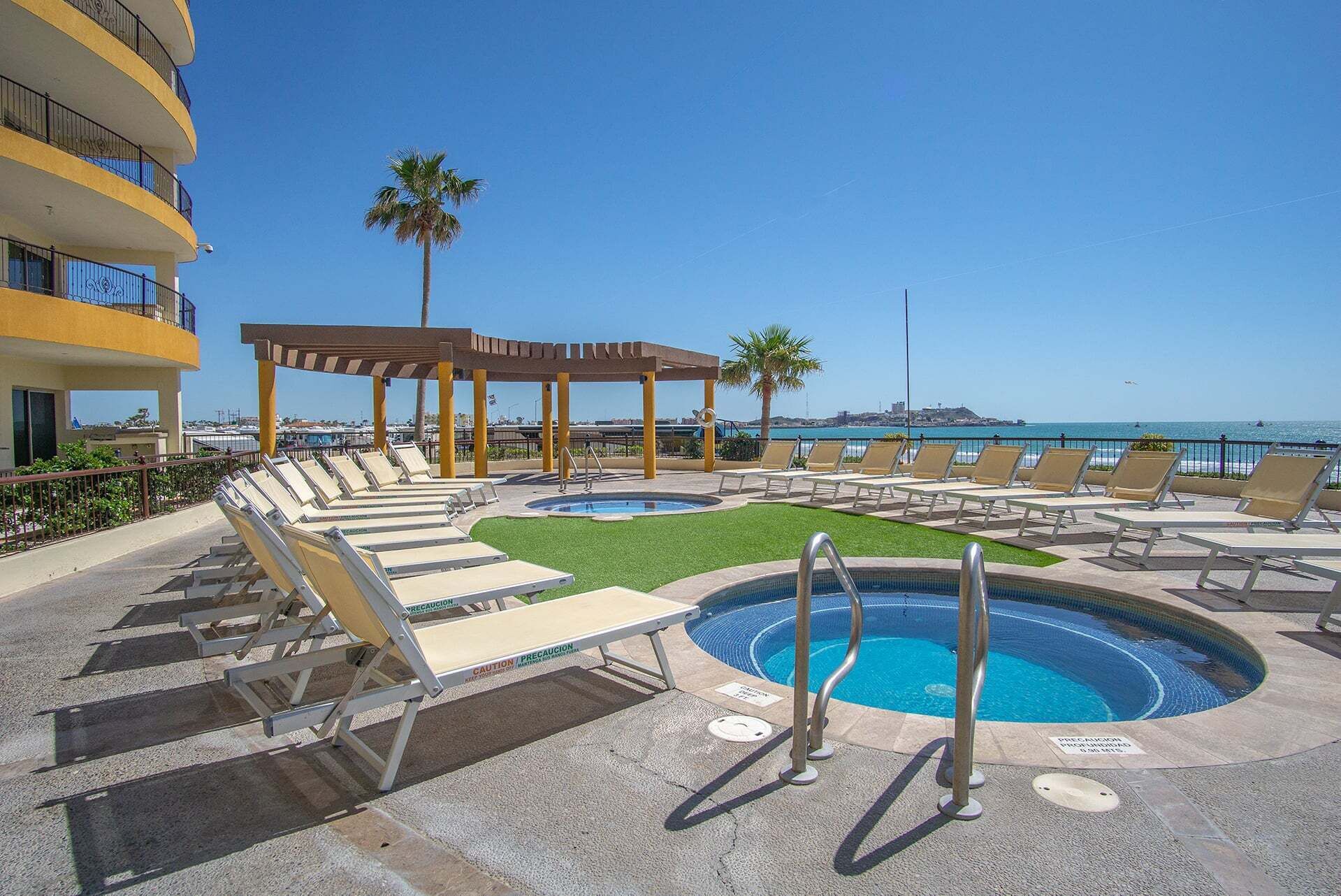 A pool area with lounge chairs, a small pool, and a view of the ocean.