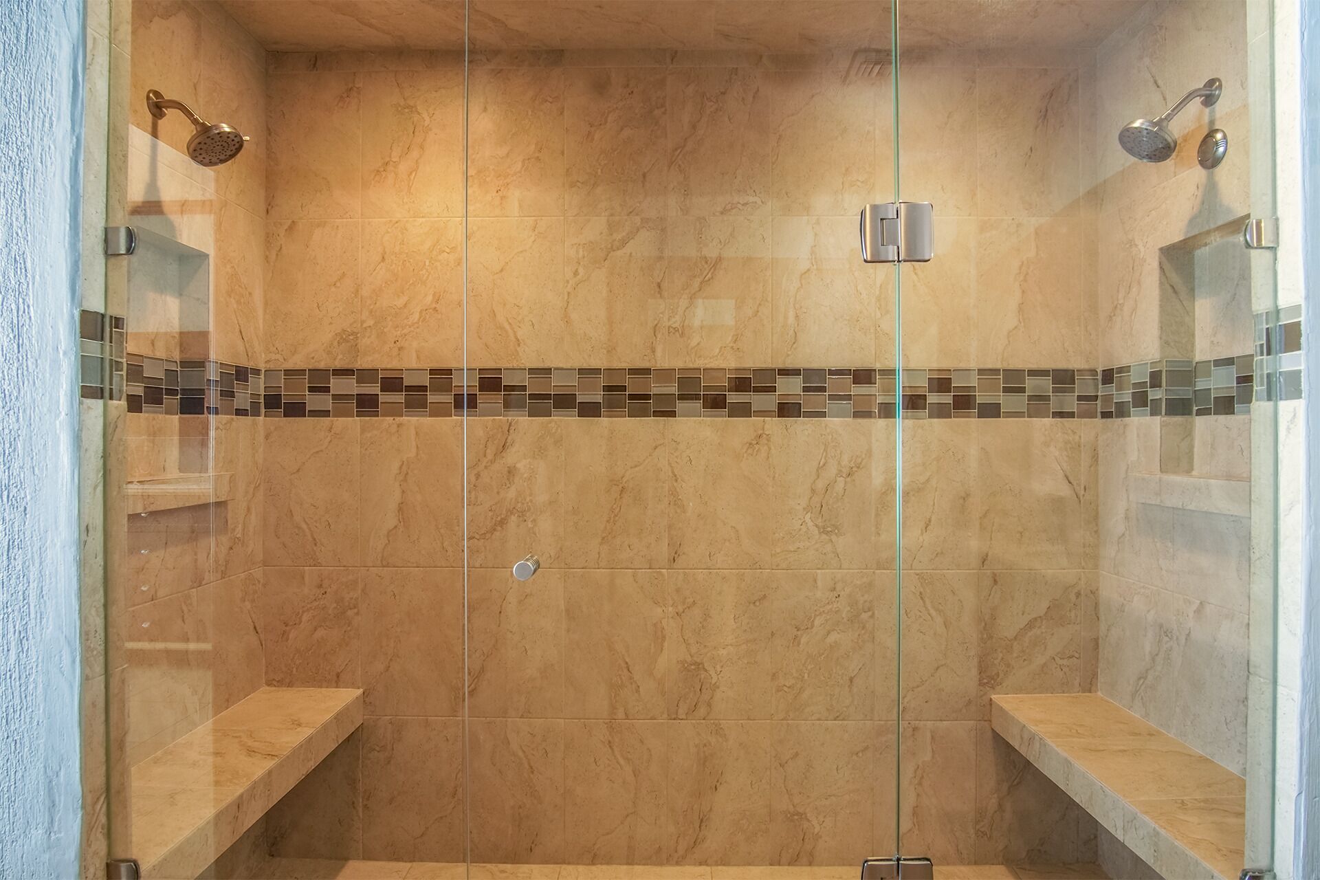 Ducha con paredes de cristal, suelo de baldosas y un borde de mosaico.