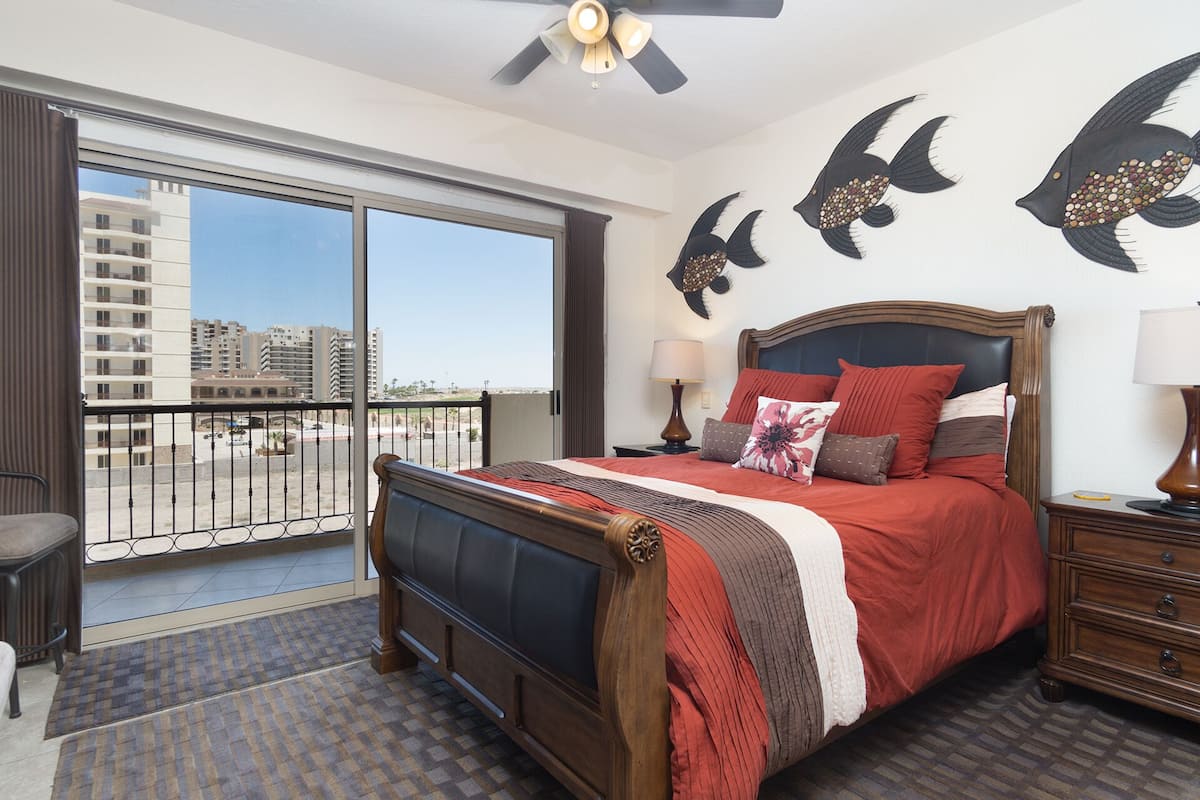 Une chambre d’hôtel avec un grand lit, un balcon offrant une vue sur les immeubles et un décor mural représentant des poissons.