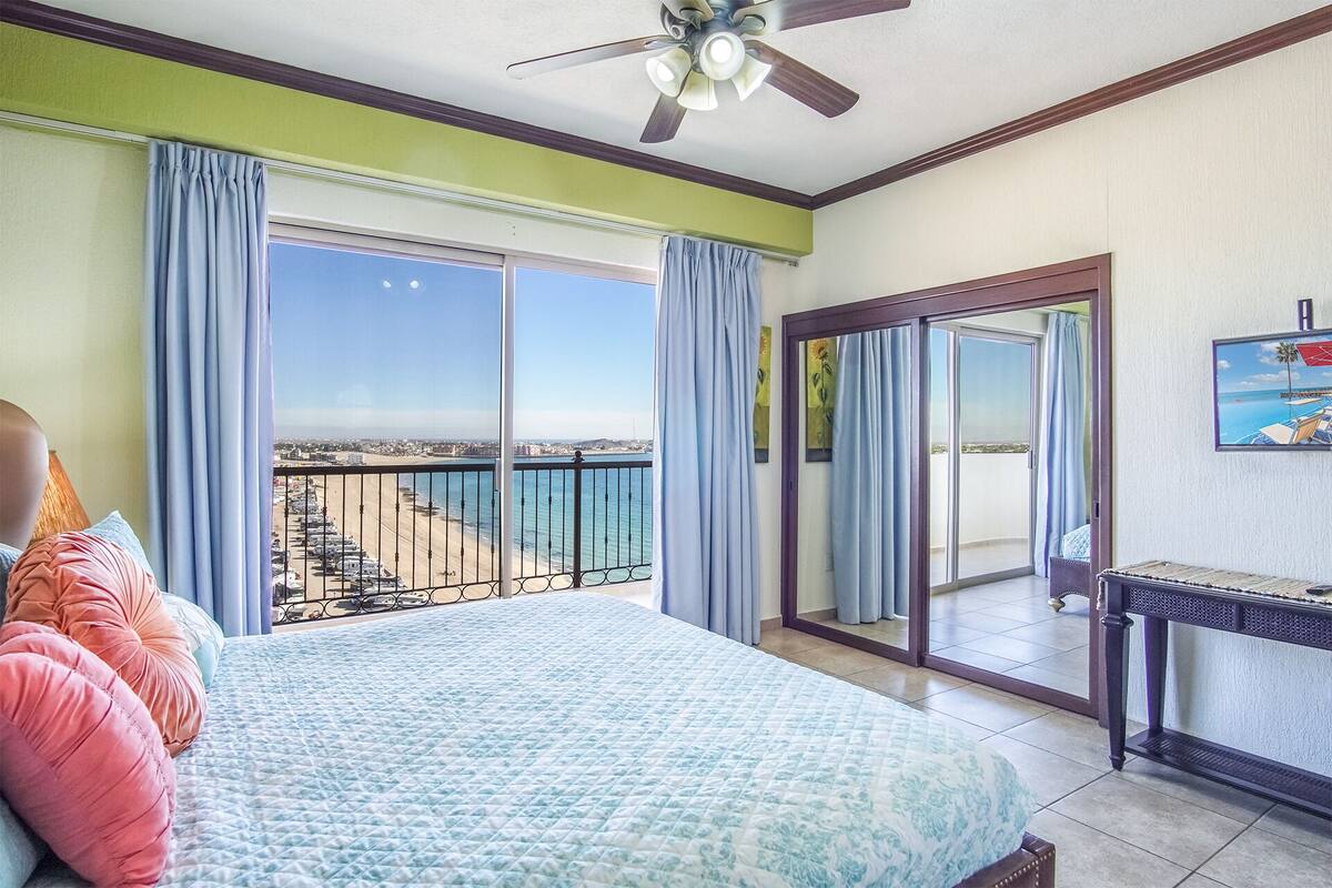 Une chambre d’hôtel avec un lit, un balcon donnant sur la plage, un ventilateur de plafond et un téléviseur fixé au mur.