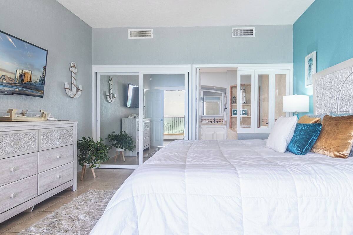 Een slaapkamer met een groot bed, een dressoir, een spiegel en uitzicht op de badkamer.