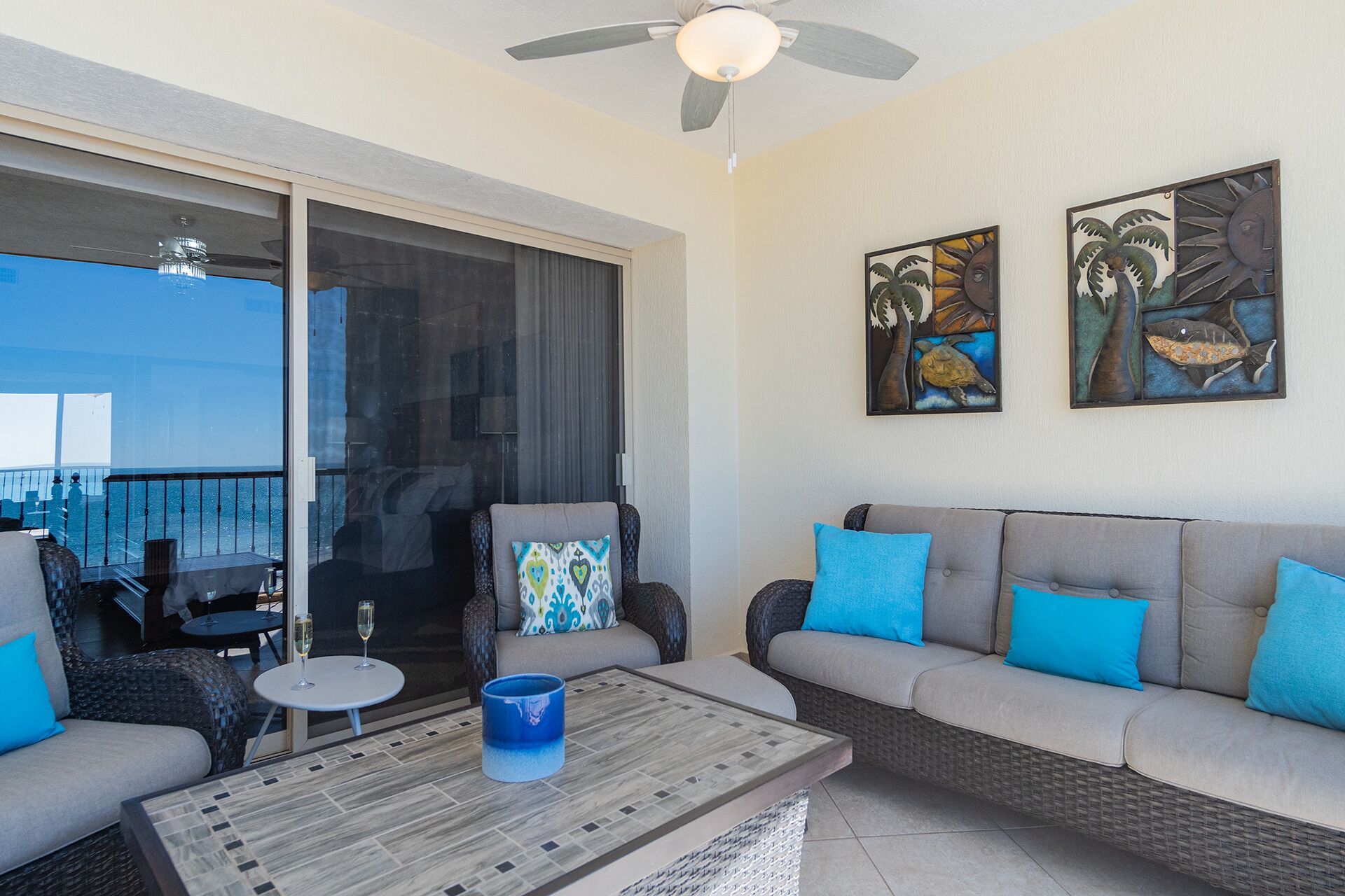A balcony with a view of the ocean, a sofa with blue cushions, and two wall-mounted artworks.