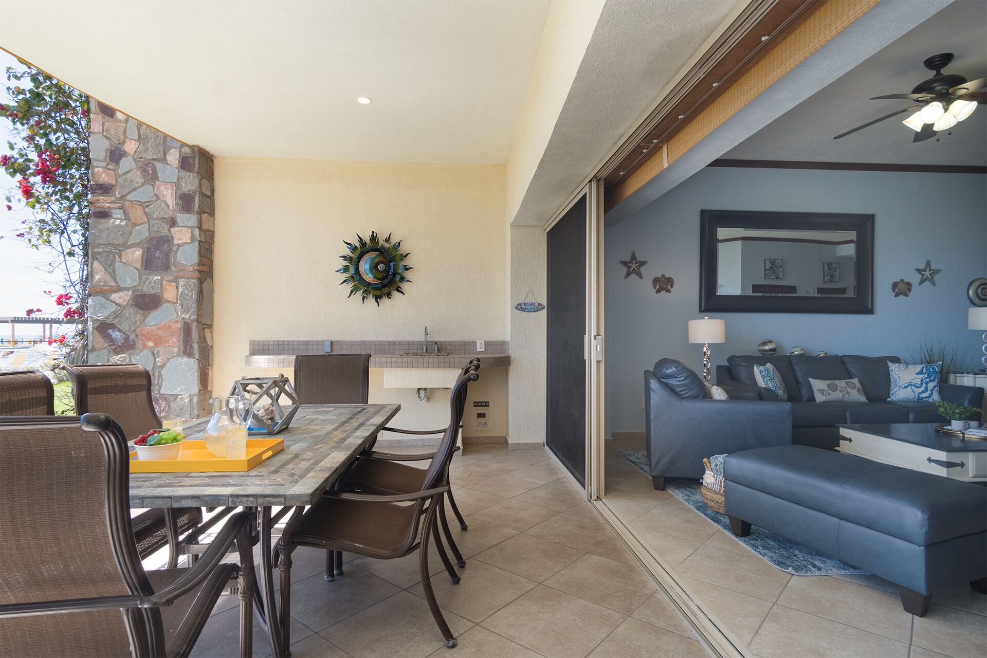 A dining area with a table and chairs, a kitchen with a sink, and a living room with a sofa and a ceiling fan.