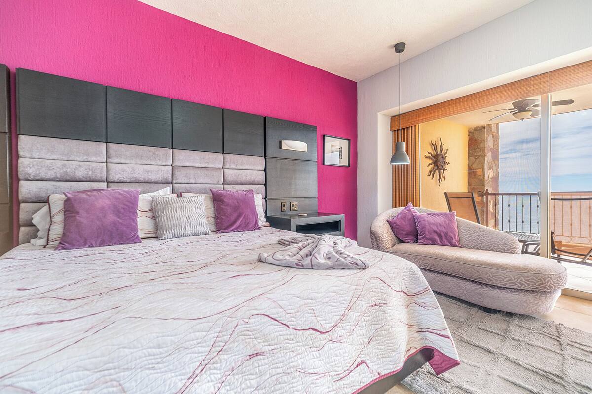Een slaapkamer met een groot bed, nachtkastje, stoel en balkon met uitzicht.