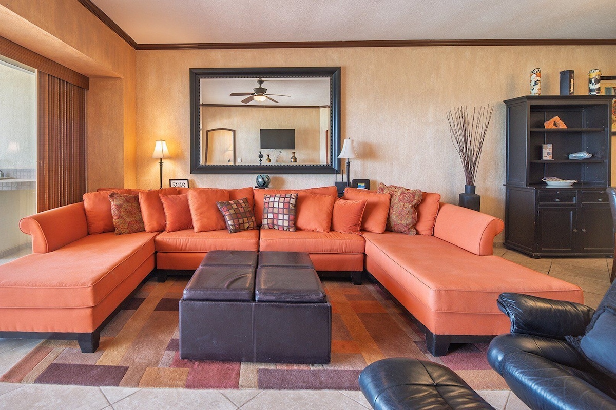 A living room with a sectional sofa, a black ottoman, a black leather armchair, and a dark wooden cabinet.