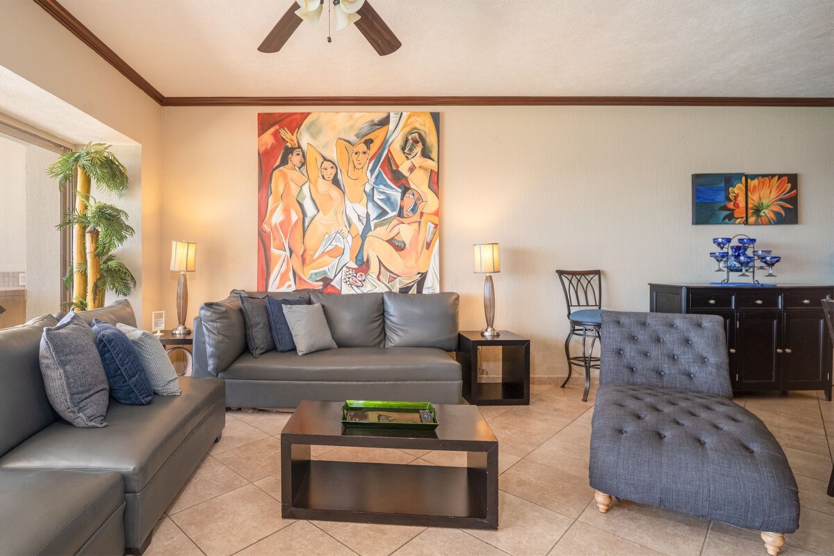 A modern living room with a grey sofa, a grey armchair, a coffee table, and a painting on the wall.