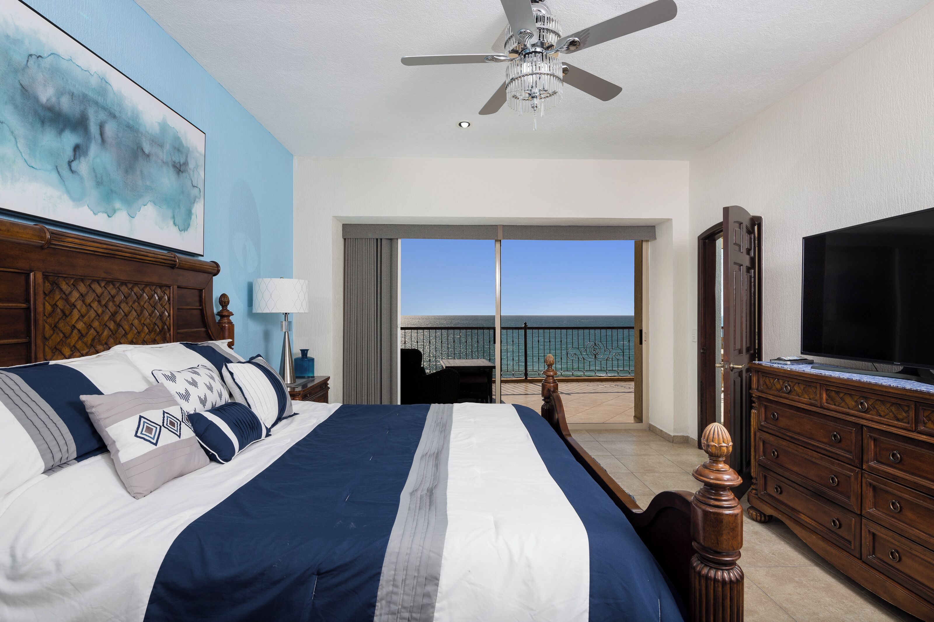 Une chambre d’hôtel avec un grand lit, un ventilateur de plafond, une télévision et un balcon avec vue sur l’océan.