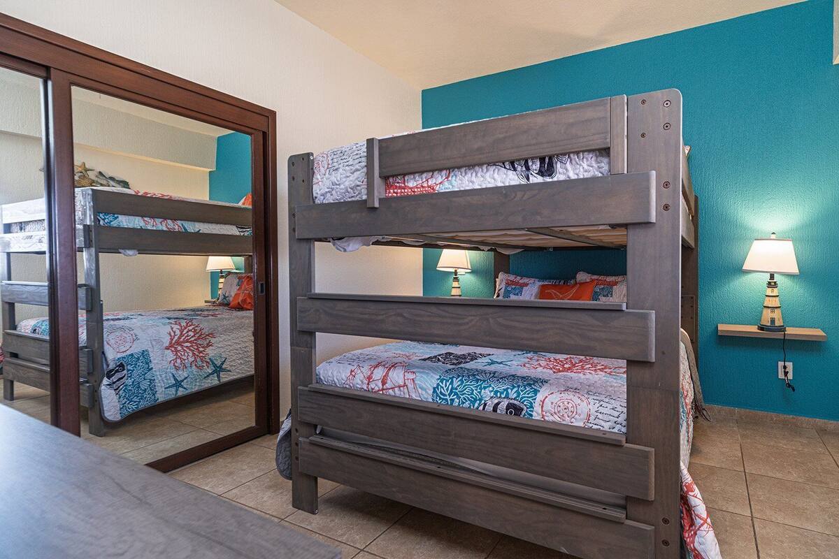 Een stapelbed met een bedsprei met dessin, een nachtkastje met een lamp, en een wand in teal kleur.
