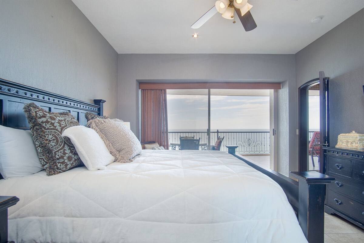 Een slaapkamer met een groot bed, een plafondventilator, een dressoir en een balkon met tuinmeubilair.