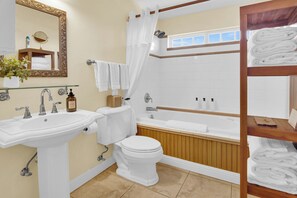 Ein Badezimmer mit Waschbecken, Toilette und Badewanne. Handtücher und Toilettenartikel befinden sich in den Regalen.