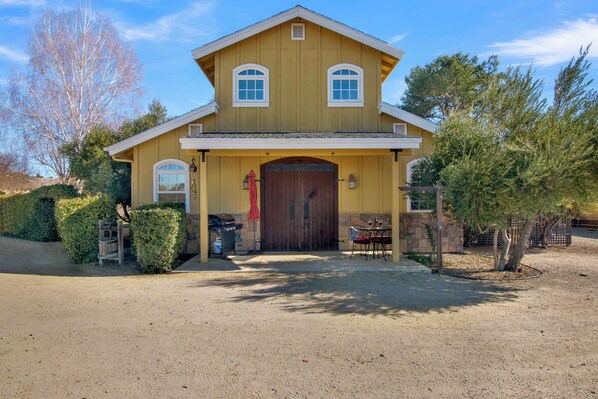Ein zweistöckiges Haus mit Veranda, einer großen Holztür und einer kleinen Terrasse mit Tisch und Stühlen.