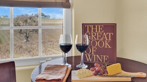 Een tafel met een boek getiteld 'The Great Book of Wine', twee glazen rode wijn, een kaasplank met druiven en een gevouwen servet.