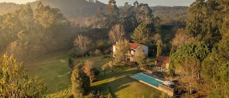 A large house with a swimming pool, surrounded by lush greenery and hills.