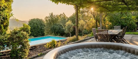 Ein Whirlpool, umgeben von einem Garten mit Schwimmbad und Holzmöbeln.