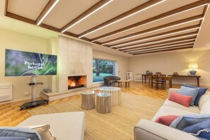 A modern living room with a fireplace, comfortable seating, a flat-screen TV, and a large window offering a view of the outdoors.