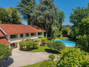 A two-story house with a swimming pool, surrounded by lush greenery and trees.