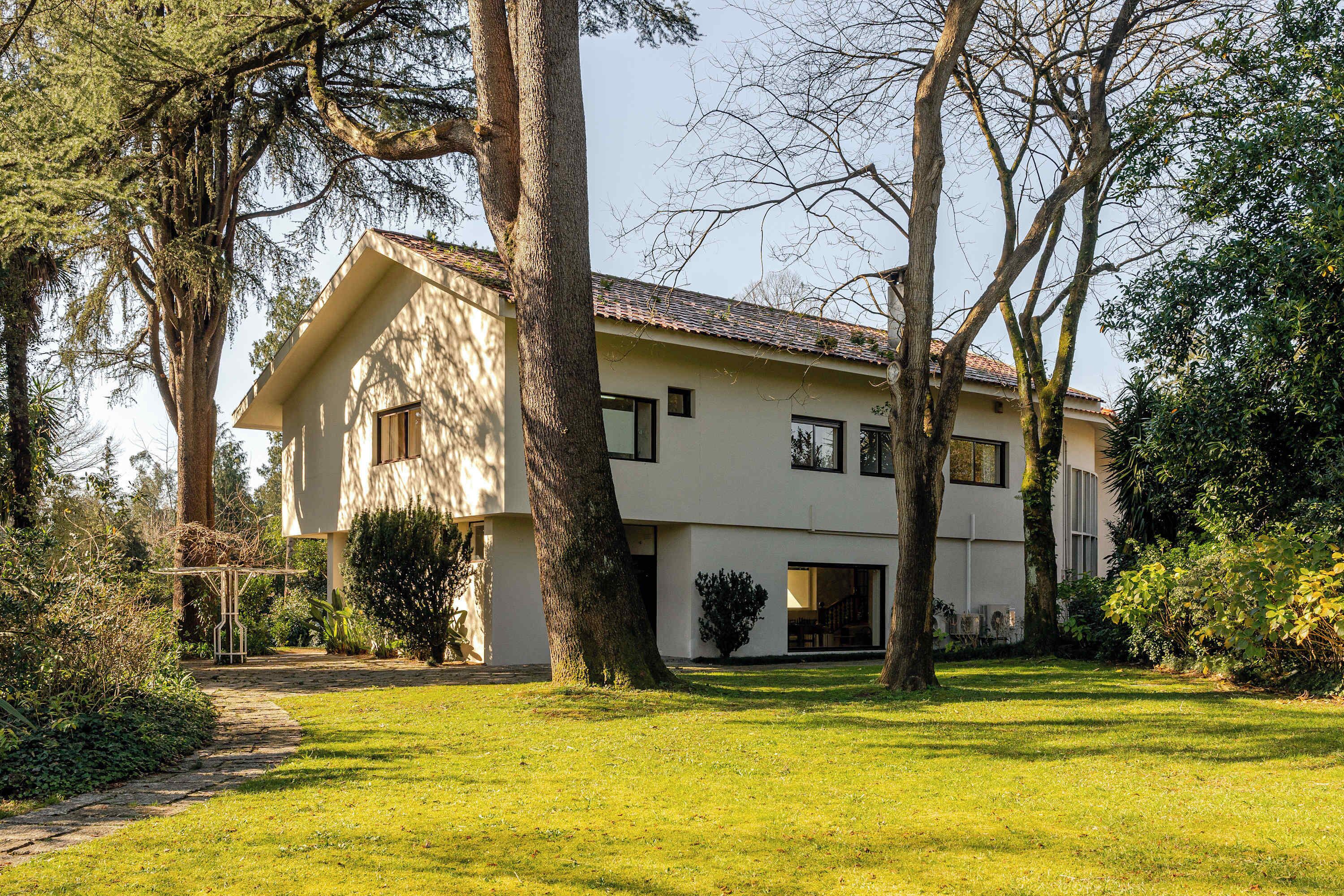 Ein zweistöckiges Haus mit geneigtem Dach, umgeben von Bäumen und einem gepflegten Rasen.