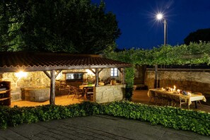 A rustic outdoor dining area with stone walls, wooden furniture, and a table set for a meal.