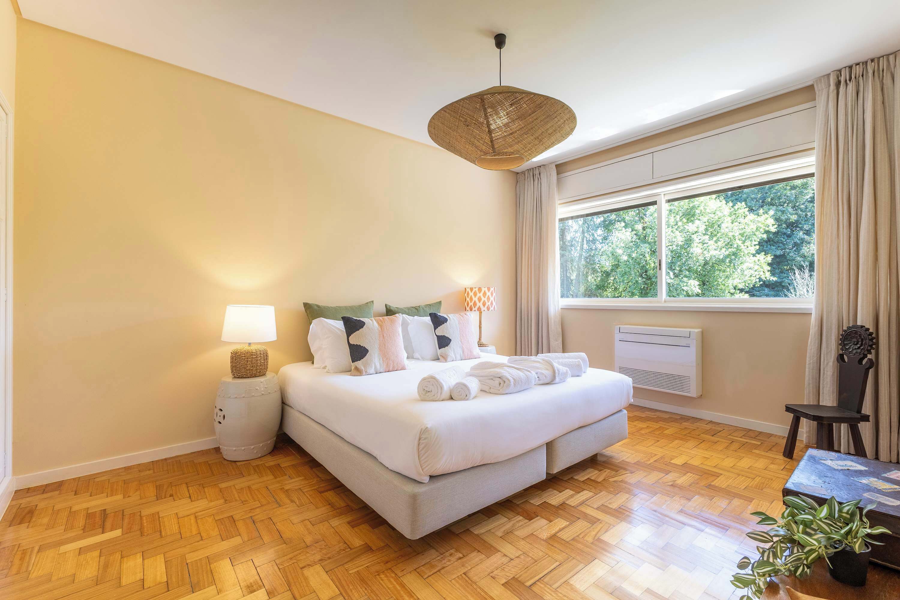 Ein Hotelzimmer mit einem großen Bett, einem Nachttisch mit Lampe, einem Fenster mit Vorhängen, einem Heizkörper und einem Holzboden.