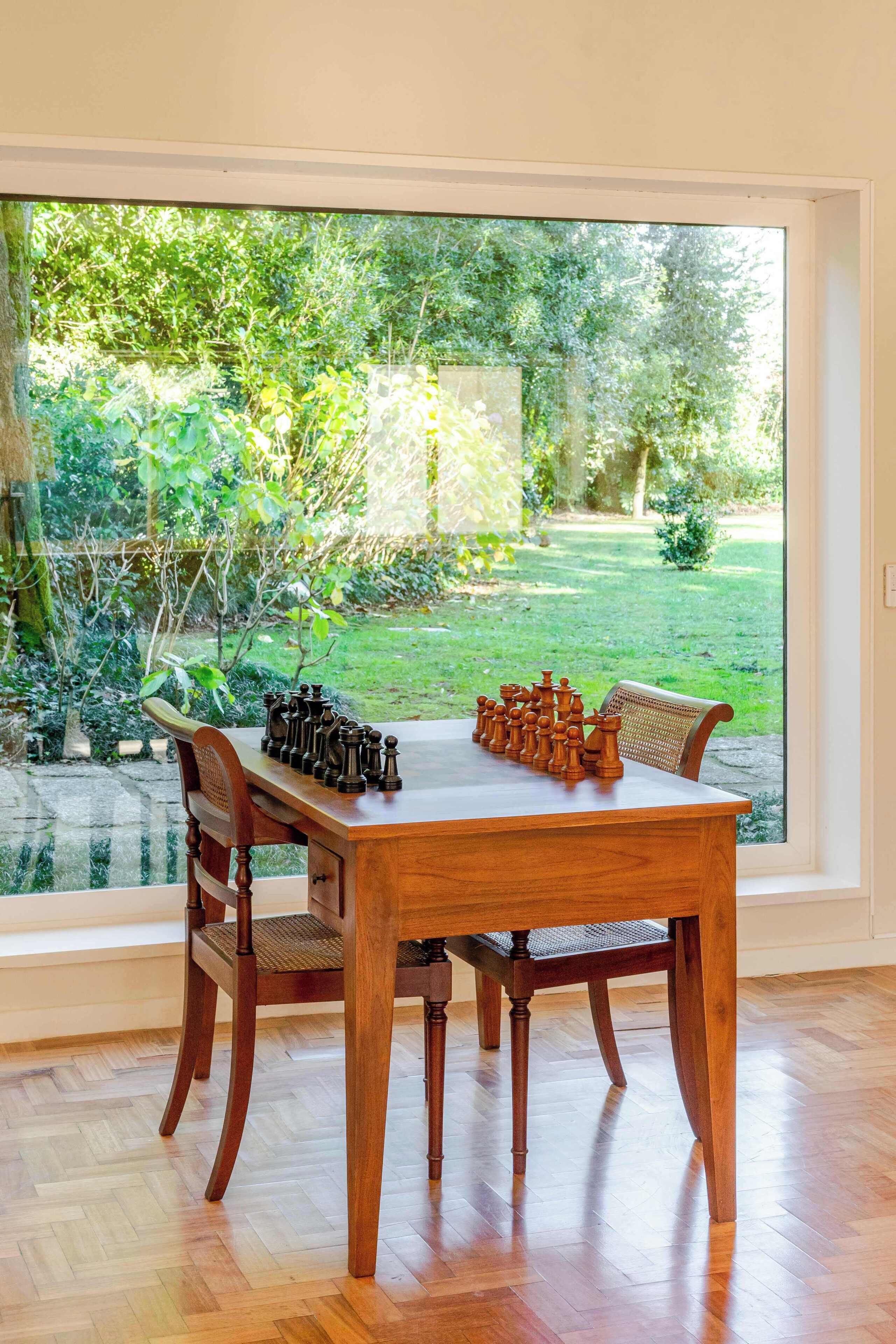 Ein Holztisch mit Schachspiel in einem Raum mit großem Fenster und Blick auf einen Garten.