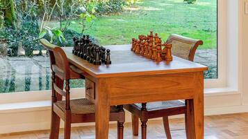 A wooden dining table with chess set in a room with a large window overlooking a garden.