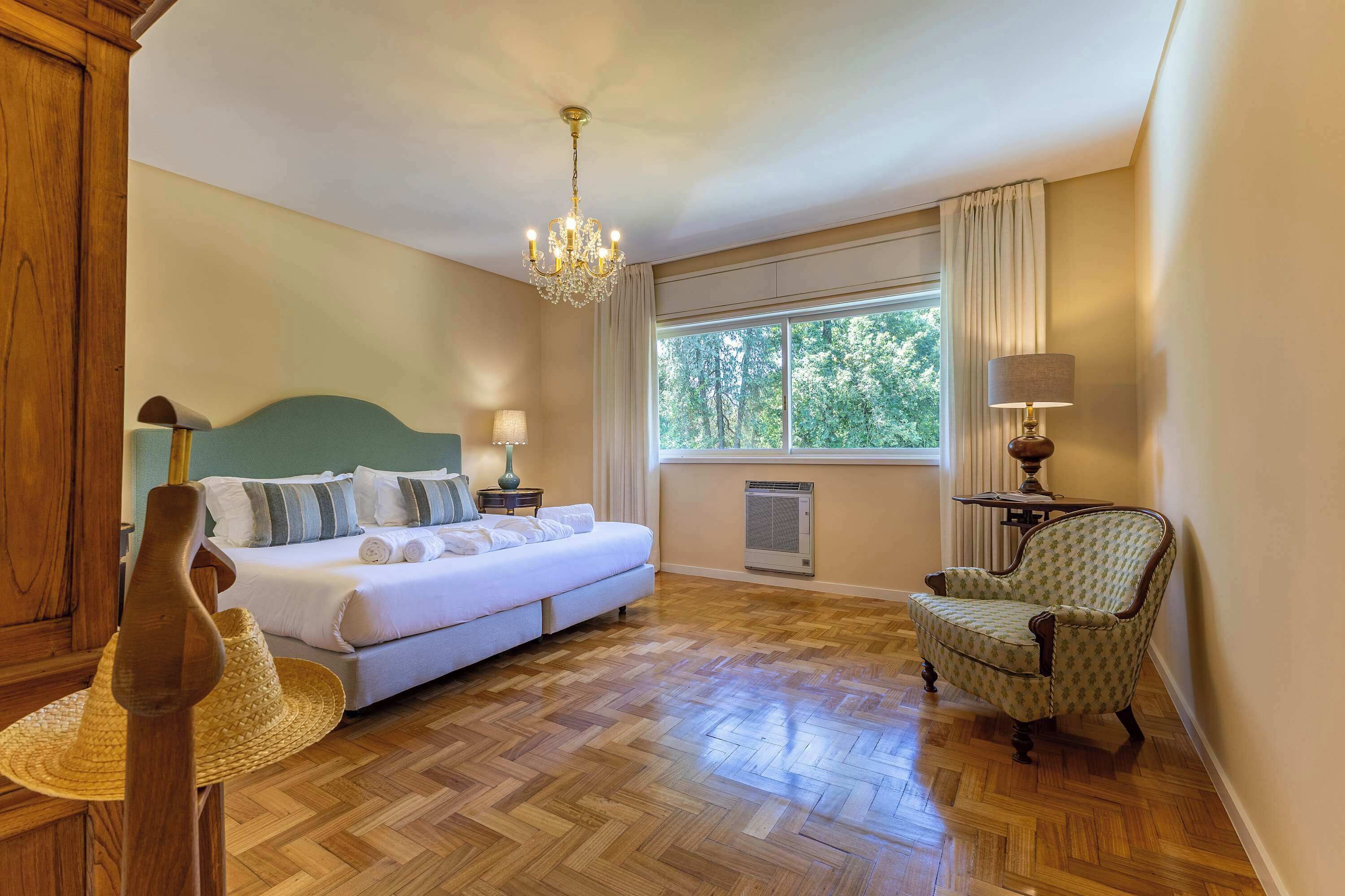 Habitación de hotel con cama, una silla, una mesa, ventana con cortinas, candelabro y aire acondicionado instalado en la pared.