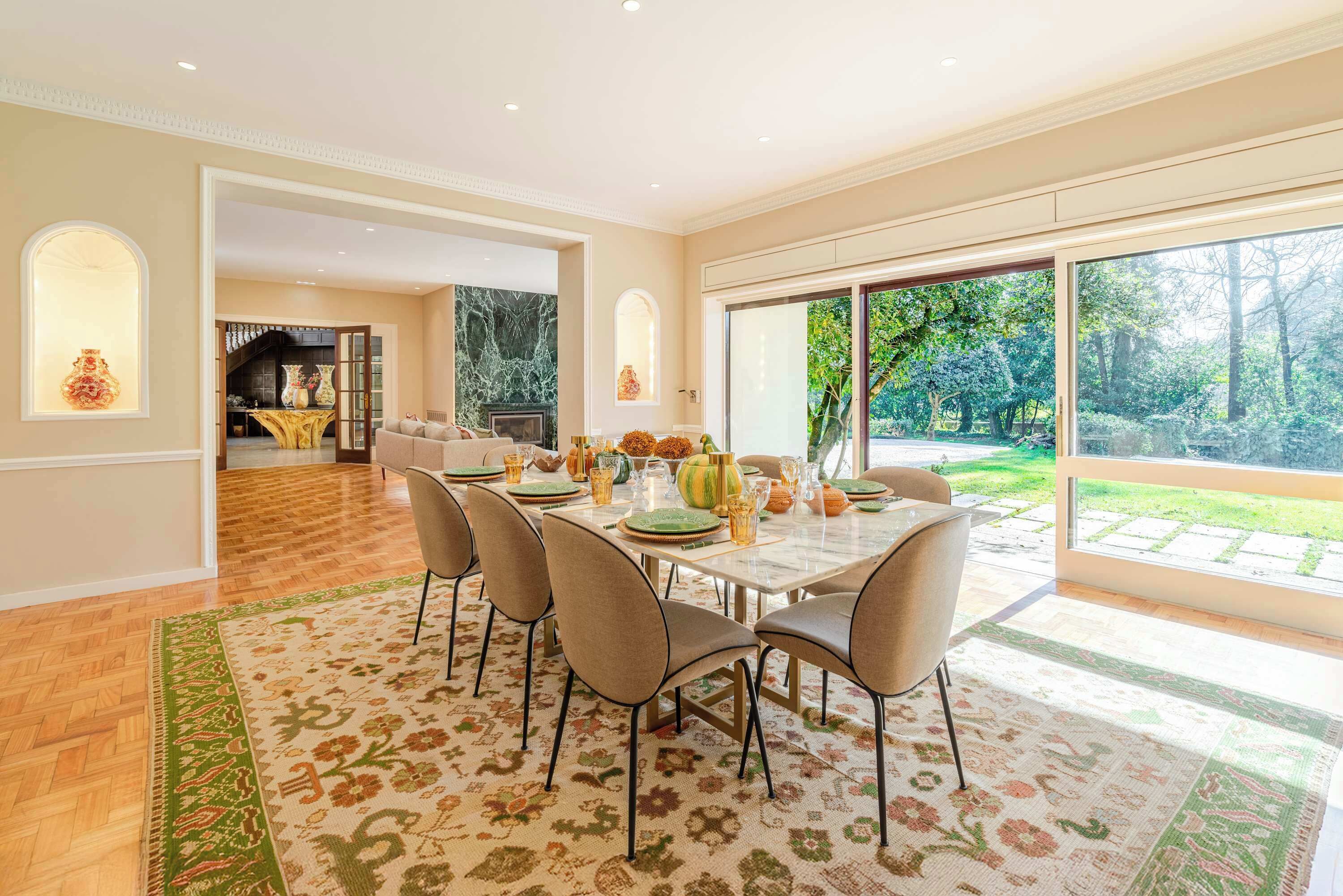 Un coin repas avec une table dressée pour quatre personnes, une cheminée et une vue sur un jardin grâce à de grandes fenêtres.