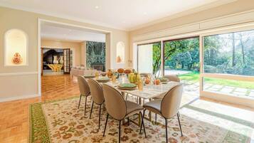 Un coin repas avec une table dressée pour quatre personnes, une cheminée et une vue sur un jardin grâce à de grandes fenêtres.