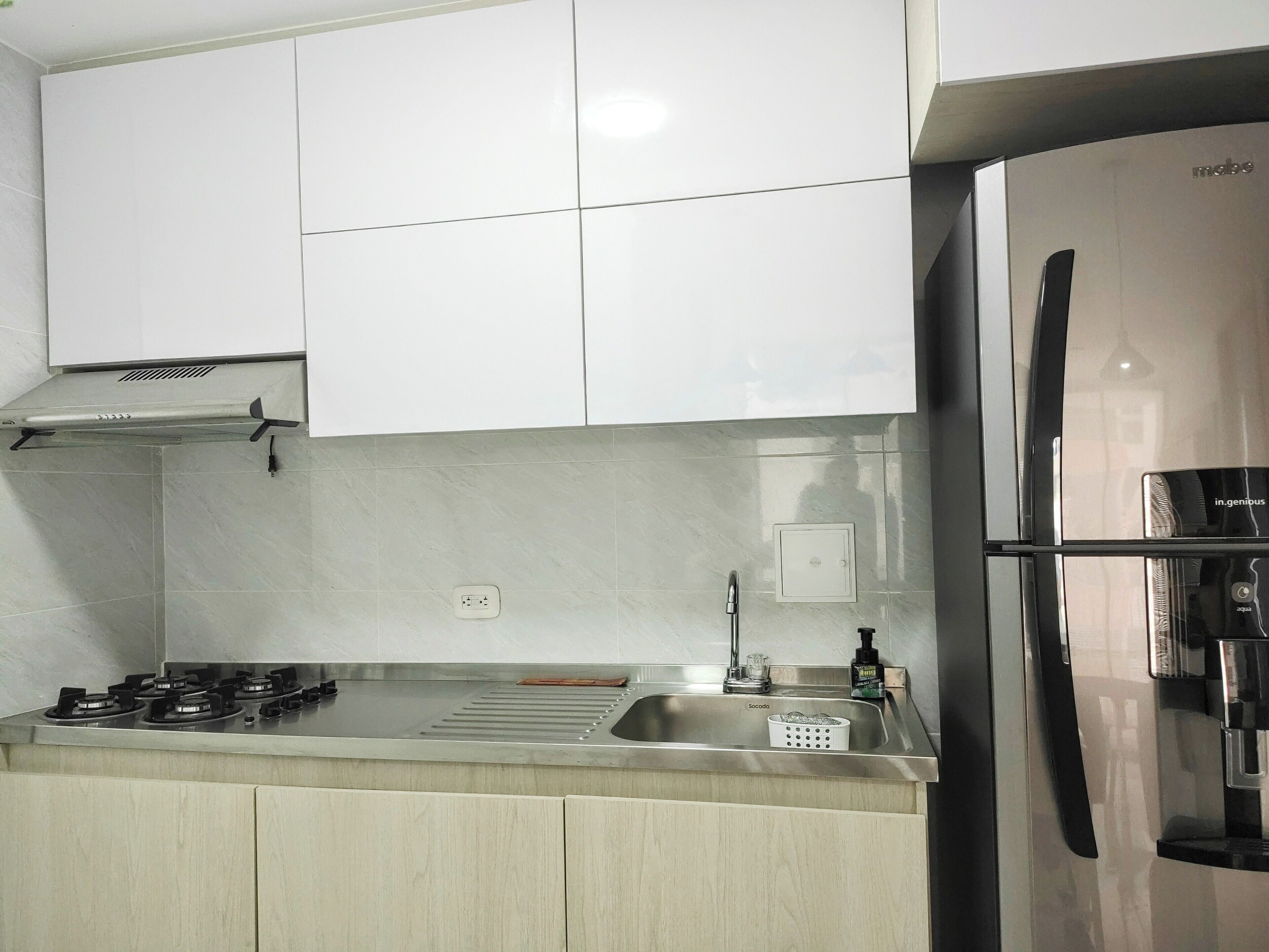 Una cocina moderna con armarios blancos, un refrigerador de acero inoxidable y una estufa a gas.
