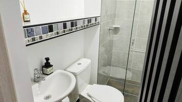 Un baño con lavamanos blanco, inodoro y cabina de ducha de vidrio.