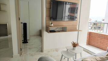 Una sala de estar moderna con un televisor de pantalla plana montado en un estante de madera, una mesita con una planta en maceta y un sofá gris.