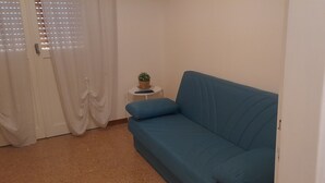 A blue sofa in a room with a small round table, a potted plant, and a white wall. - Ravenna Suite: apartment close to the center and major monuments! (Ravenna)