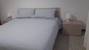 A neatly made bed with a light-colored bedspread, two pillows, and two bedside tables with lamps. - Ravenna Suite: apartment close to the center and major monuments! (Ravenna)