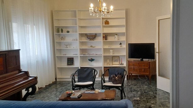 A living room with a piano, two chairs, a coffee table, a TV, and a bookshelf. - Ravenna Suite: apartment close to the center and major monuments! (Ravenna)