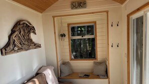A cozy room with a wooden ceiling, a built-in bench with cushions, a window with a view of trees, and a sign above the window that reads "SURF".