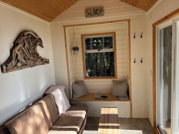Una habitación acogedora con techo de madera, un banco empotrado con cojines, una ventana con vistas a árboles y un cartel sobre la ventana que dice "SURF".
