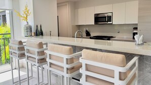Cozinha moderna com ilha central, banquetas, eletrodomésticos de aço inoxidável e vista para o verde lá fora.
