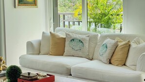 Um sofá branco com almofadas decorativas, uma mesinha com uma caixa vermelha e um quadro na parede.