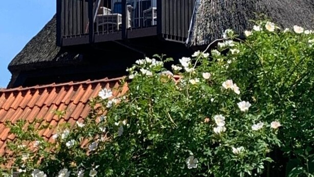 Une maison avec un toit à forte pente, un balcon doté d’une balustrade et un toit recouvert de tuiles rouges.
