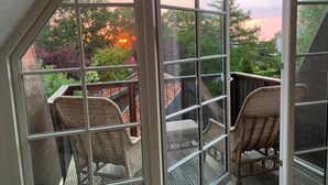 Un balcon avec des fauteuils en osier et une vue sur les arbres et le coucher de soleil.