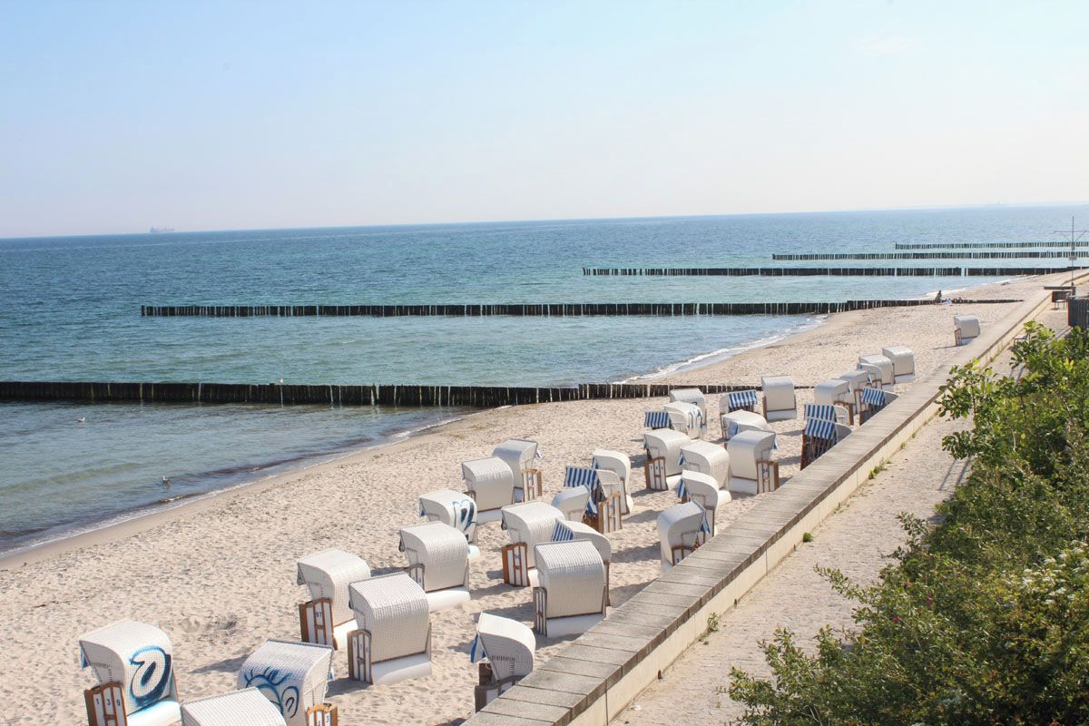 A beach with rows of white beach chairs and umbrellas, a wooden walkway, and a pier extending into the sea.