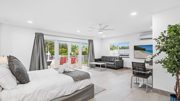 A modern bedroom with a bed, a desk, and a chair. There is a balcony with a view of the outdoors.