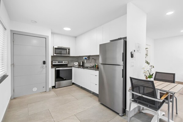 A modern kitchen with white cabinets, stainless steel appliances, and a dining area with a table and chairs.