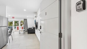 A modern hotel room with a kitchenette, a flat-screen TV mounted on the wall, and an 'EXIT' sign above the door.