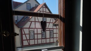 A window with a view of a traditional half-timbered house, a heart-shaped decoration, and a white vase with a ribbon.