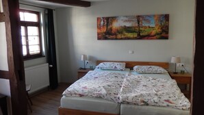 A bedroom with a wooden bed, two bedside tables with lamps, a radiator, and a window with curtains.