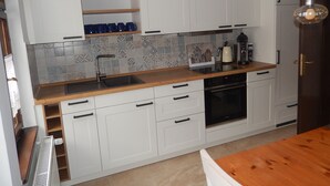 A modern kitchen with white cabinets, a wooden countertop, a built-in oven, and a coffee maker.