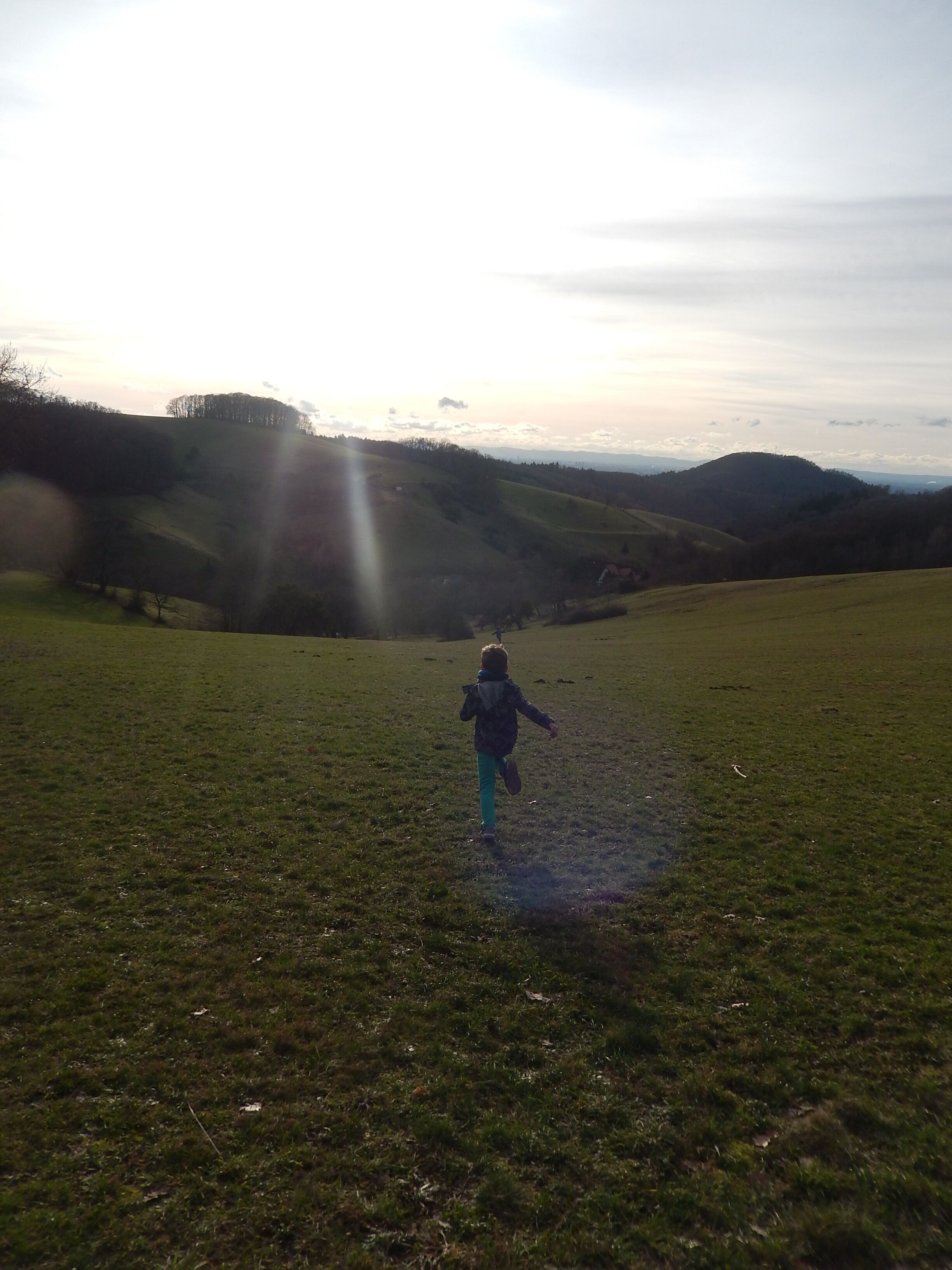 Un enfant court dans un champ herbeux, avec un paysage vallonné en arrière-plan.