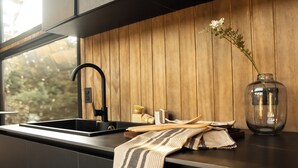 Una cocina moderna con un lavamanos negro, un panel trasero de madera y un florero con una flor en la encimera.